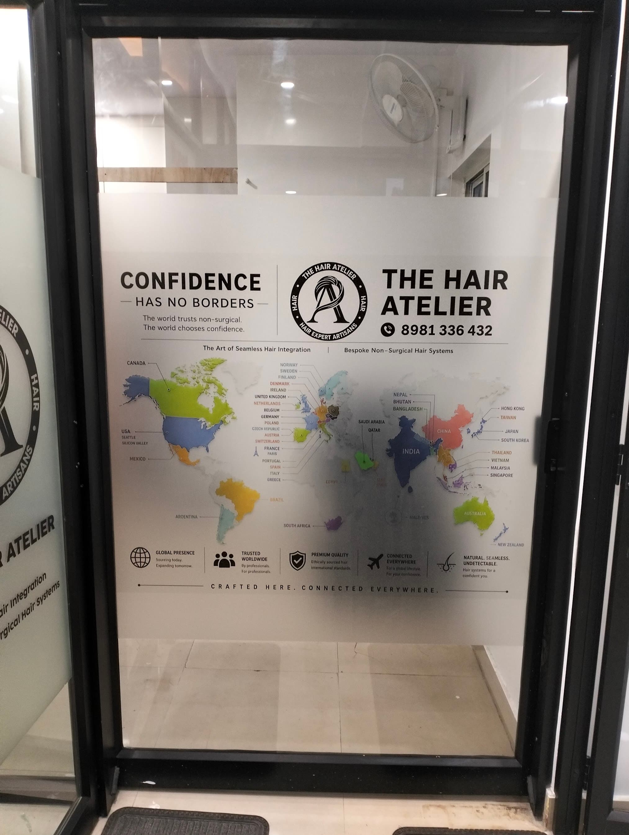 Glass entrance door of THE HAIR ATELIER at Siri Arcade, Whitefield, showing the salon logo, the phone number 8981 336 432 and the line Confidence Has No Borders